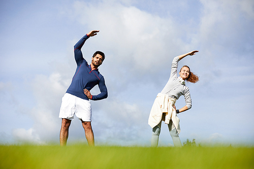 Happy young active couple in sportswear exercising on green grass on summer weekend