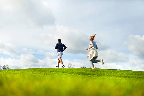 Active young couple in sportswear jogging on large green field in natural environment