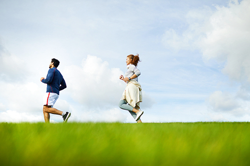 Active couple jogging on green field and enjoying their outdoor training