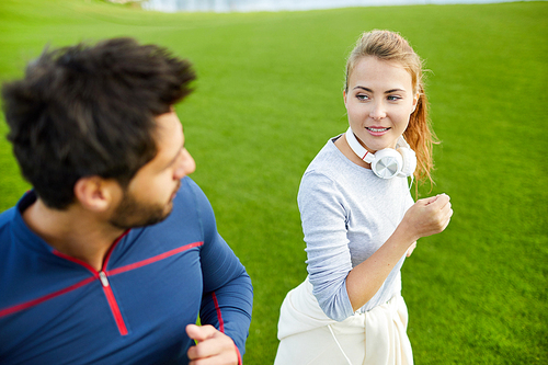 Active young woman with headphones around neck talking to her boyfriend while jogging in the morning
