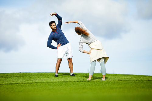 Young man and woman standing on green lawn in front of one another while exercising