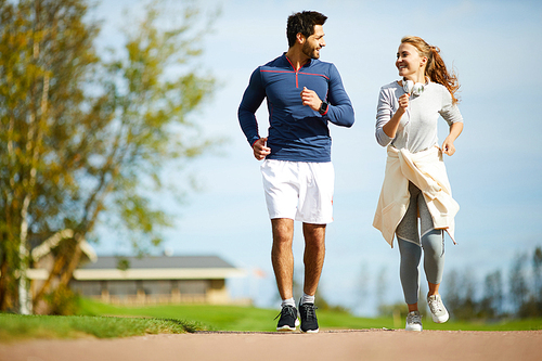 Amorous young couple in activewear running in rural environment on sunny day
