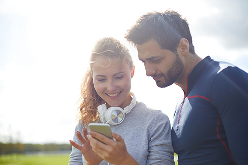 Happy girl showing her boyfriend curious message or video in smartphone after outdoor workout