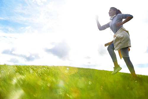 Young sportswoman in activewear jogging on green field against cloudy sky in the morning