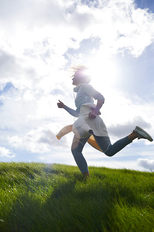 Active young woman running against skyline and sun shining among clouds on sky