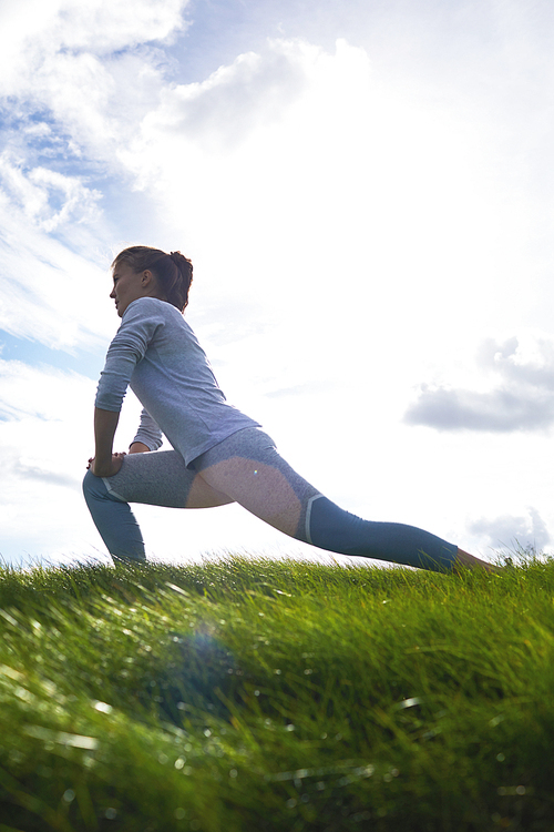 Active woman stretching her legs while doing exercise on green lawn in the morning