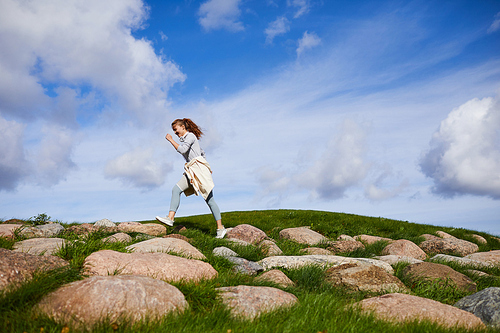 Active young woman walking down large stones against cloudy sky in the morning