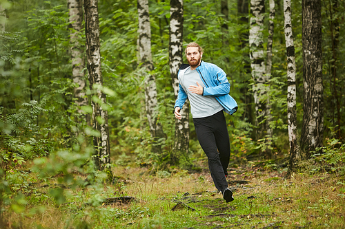 Young sportsman in activewear having jog training in the forest on summer morning