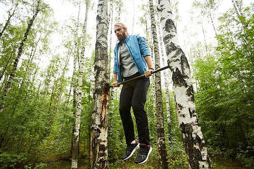 Young sportsman pulling up on gymnastics bar between two birches in the forest while exercising in the morning