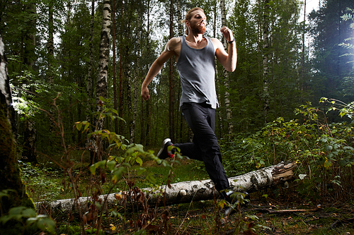 Active man in sportswear having morning run in birch forest and enjoying summer morning