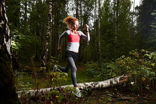 Young active sportswoman running in birch forest on summer weekend or in the morning