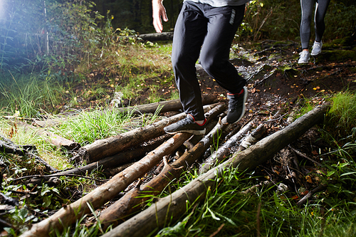 Young sporty couple in activewear moving down logs in the forest while training at leisure
