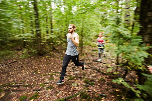 Blurry motion of young sporty couple running in the forest among green trees on summer morning