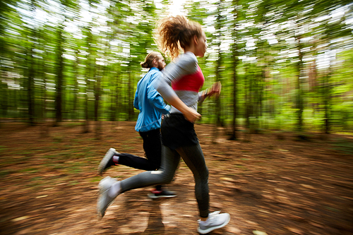 Young couple in activewear running on forest road with blurry trees on background