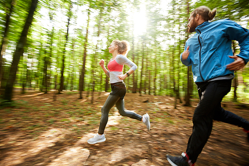 Young active man and his girlfriend jogging out in the forest on sunny day among blurred trees