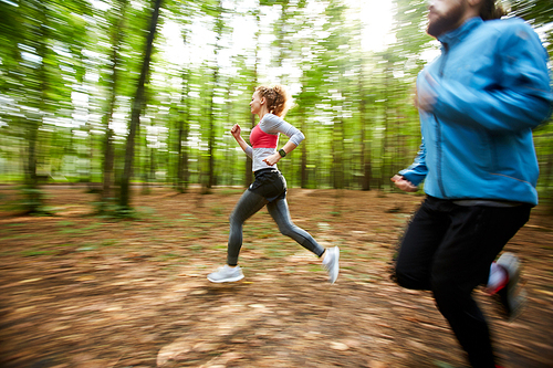 Morning training of active young couple jogging in the forest on summer day among blurry trees