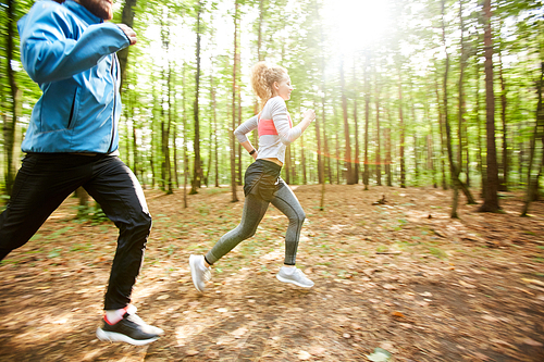 Young couple in activewear moving on the ground in the forest on sunny morning on background of blurry trees