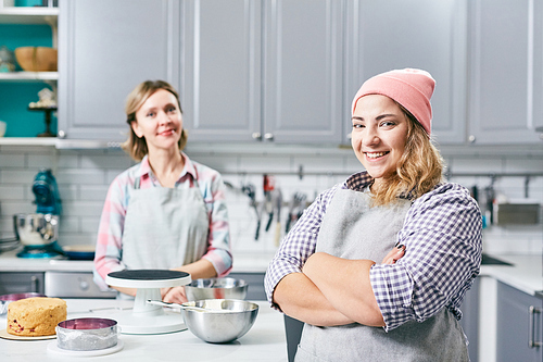 Portrait of young Caucasian female pastry cooks standing in kitchen and smiling at camera happily