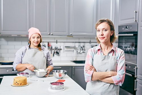 Portrait of young attractive Caucasian women in aprons standing in kitchen with pastry and 