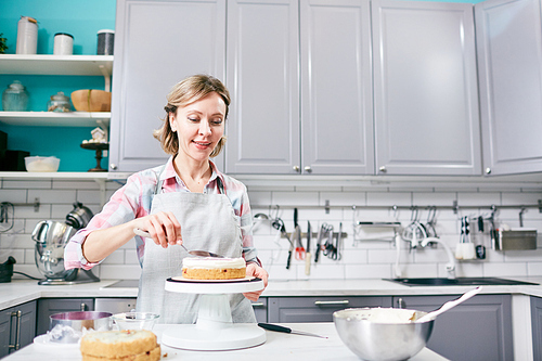 Low angle view of attractive Caucasian woman preparing appetizing cake in kitchen and smiling joyfully