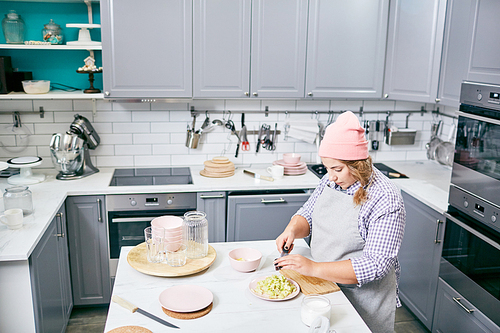 High angle view of stylish female cook in apron and hat cutting pear in modern kitchen