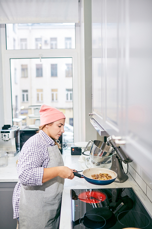 High angle view of stylish Caucasian female cook preparing dish in frying pan in modern kitchen