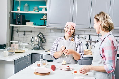 Young attractive Caucasian women cooking tasty strawberry cupcakes in modern kitchen, chatting and smiling cheerfully