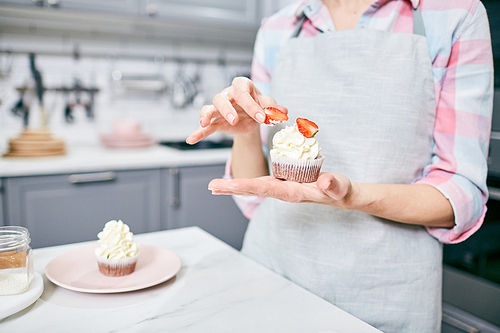 Unrecognizable woman in apron holding appetizing cupcake with cream and strawberries