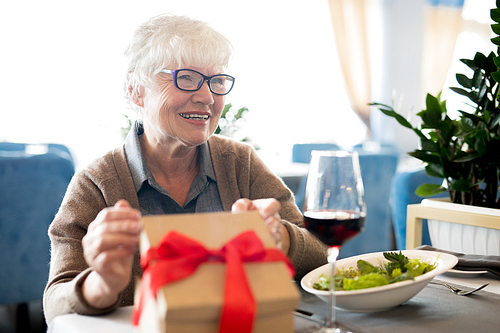 Portrait of happy senior woman receiving present while enjoying celebration sitting at table in cafe, copy space