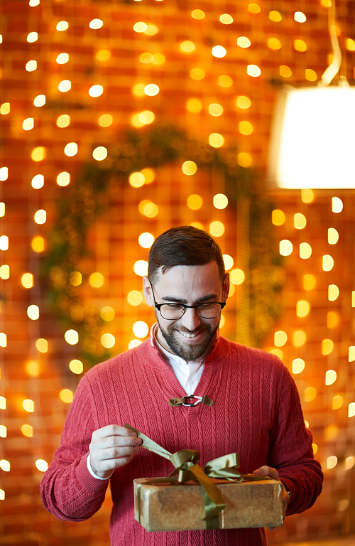 Happy businessman untying golden ribbon on top of gift-box during Christmas party in office