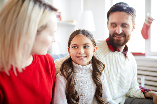 Little girl in white sweater looking at her mother during conversation while sitting between her parents