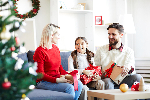 Young parents and their little daughter with giftboxes discussing what lies inside them