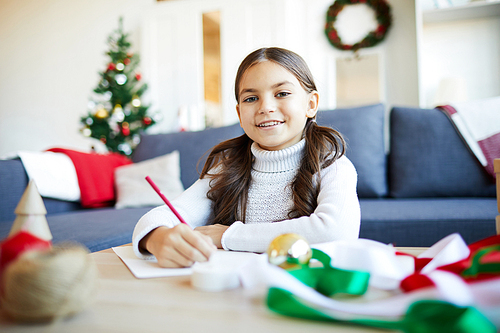 Happy girl drawing something on paper while preparing for Christmas