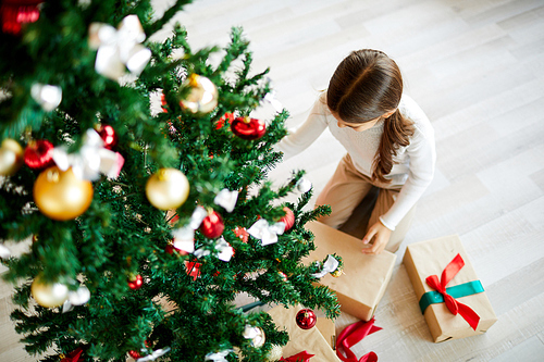 Little girl unpacking or looking for her xmas gift under decorated firtree on the floor
