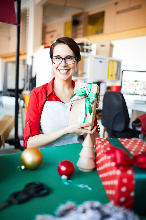 Young cheerful woman in workwear holding self-made gift packed in box