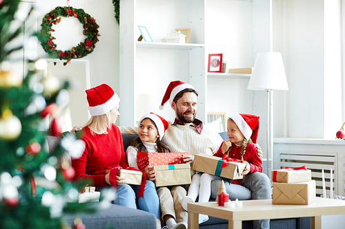 Contemporary family of four in Santa caps and casualwear relaxing on sofa on xmas eve