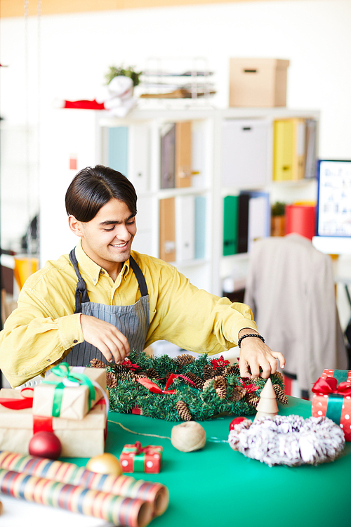 Young creative man in workwear making xmas decorations and wreath in design studio