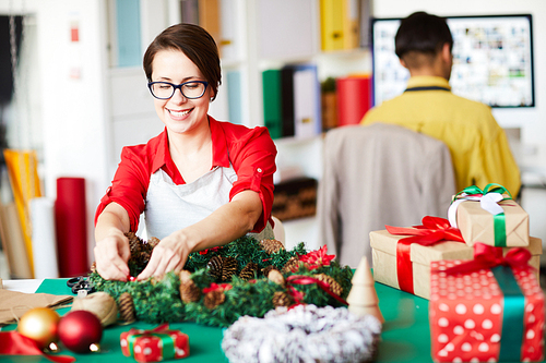 Happy young designer putting pine cones and red bows on Christmas wreath