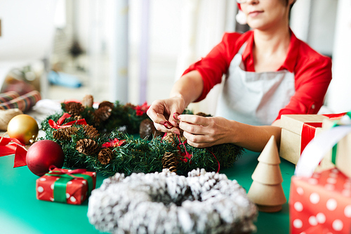 Young designer tying red ribbon on xmas wreath decorated with pine cones