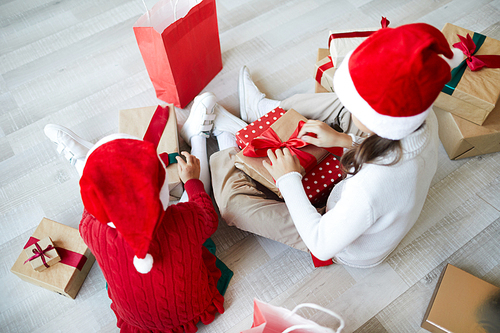 Two little Santas preparing gifts for forthcoming Christmas while sitting on the floor