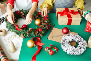 Hands of young woman finishing up with coniferous Christmas wreath while colleague helping her