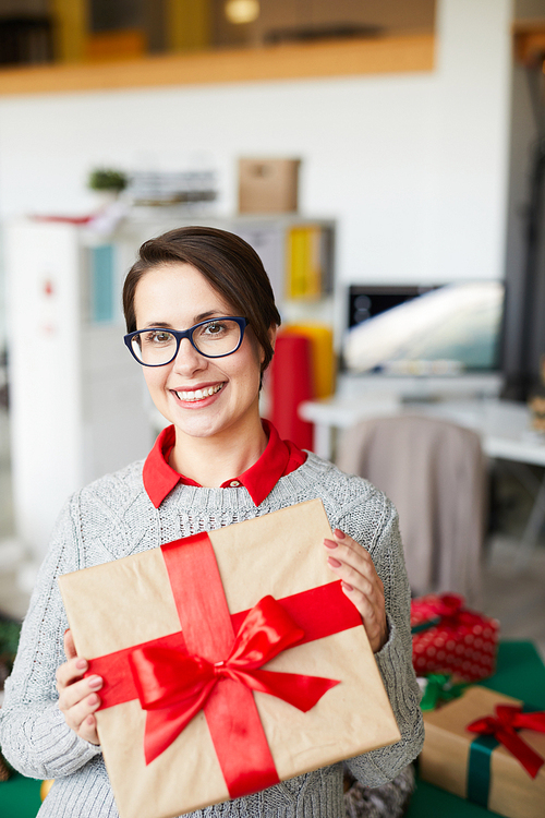 Young smiling female with packed box tied up with silk red ribbon showing it to you