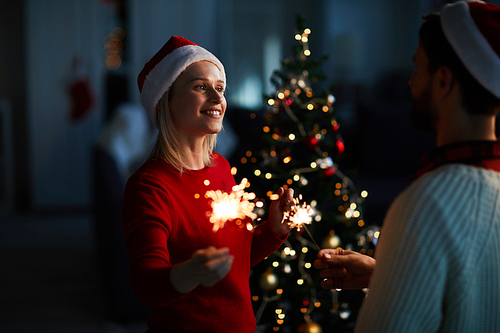 Young amorous couple with bengal lights looking at one another by Christmas tree