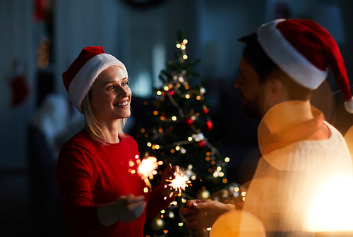 Romantic couple in Santa caps celebrating Christmas together by decorated firtree
