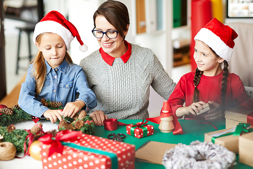 Happy young woman and little girls making Christmas wreath and decorating it with cones