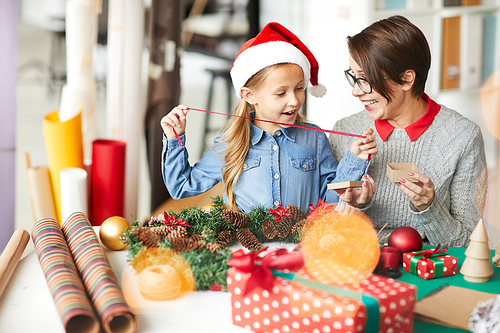 Cheerful little girl in xmas cap and her mother discussing what to put into small giftbox