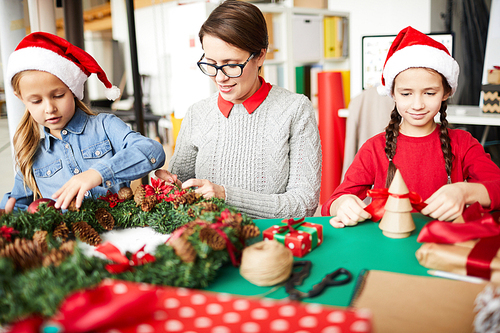 Young female and her two daughters working over Christmas stuff while sitting by table