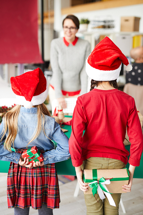 Rear view of two little girls in Santa caps hiding xmas gifts for their mother behind backs