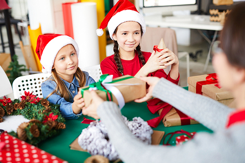 One of cute little girls taking packed xmas gift from her mother on the eve