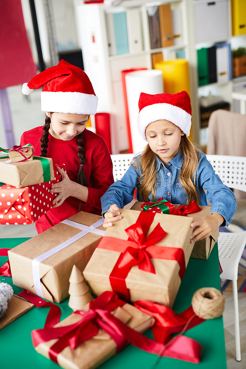 Two pretty little girls in Santa caps preparing packed giftboxes for Christmas day